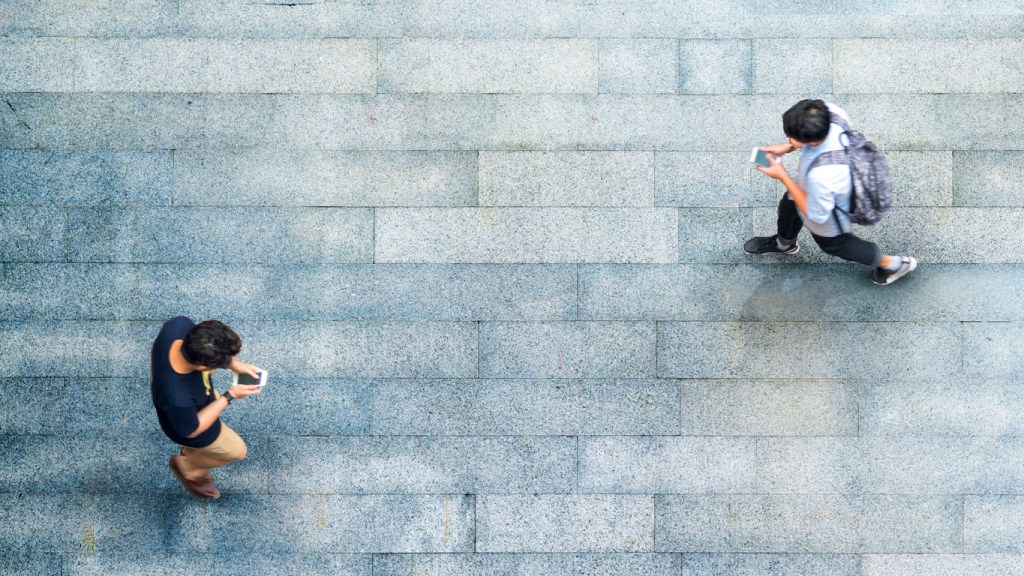 two men walking while looking at their cell phones