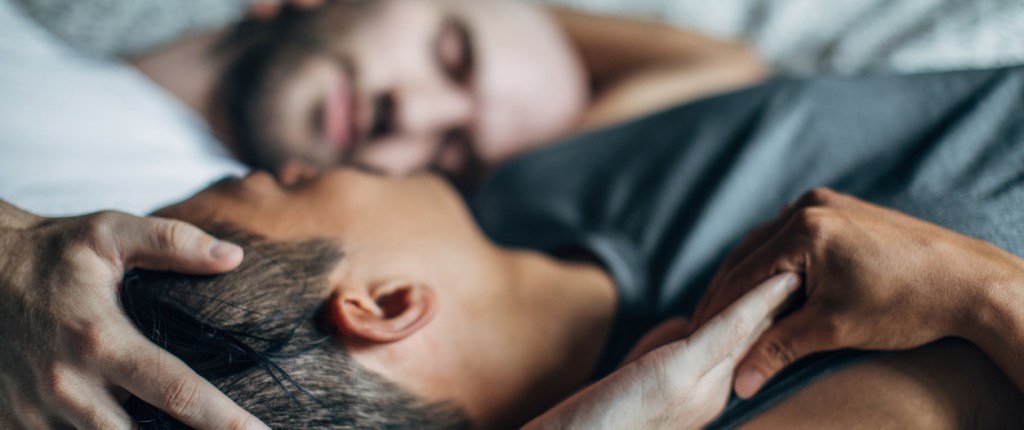 two men in bed holding hands